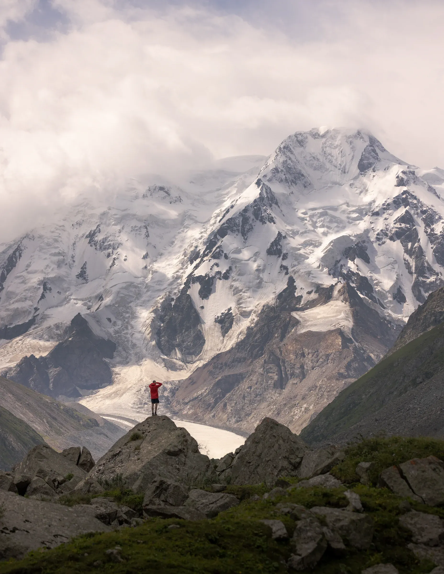 A figure in red facing a wall of snow-covered mountains