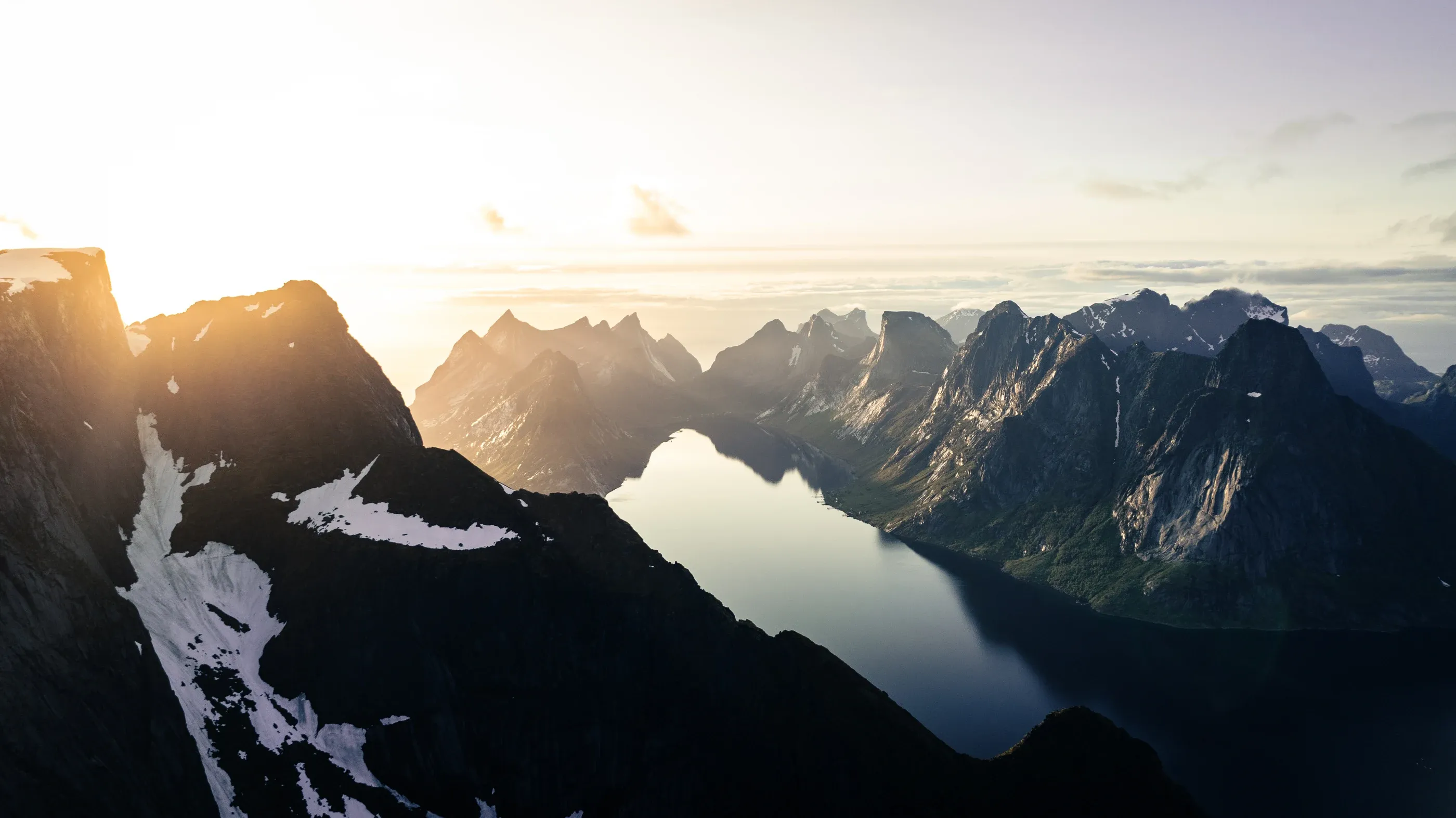Sunlight breaking over jagged peaks above a still fjord