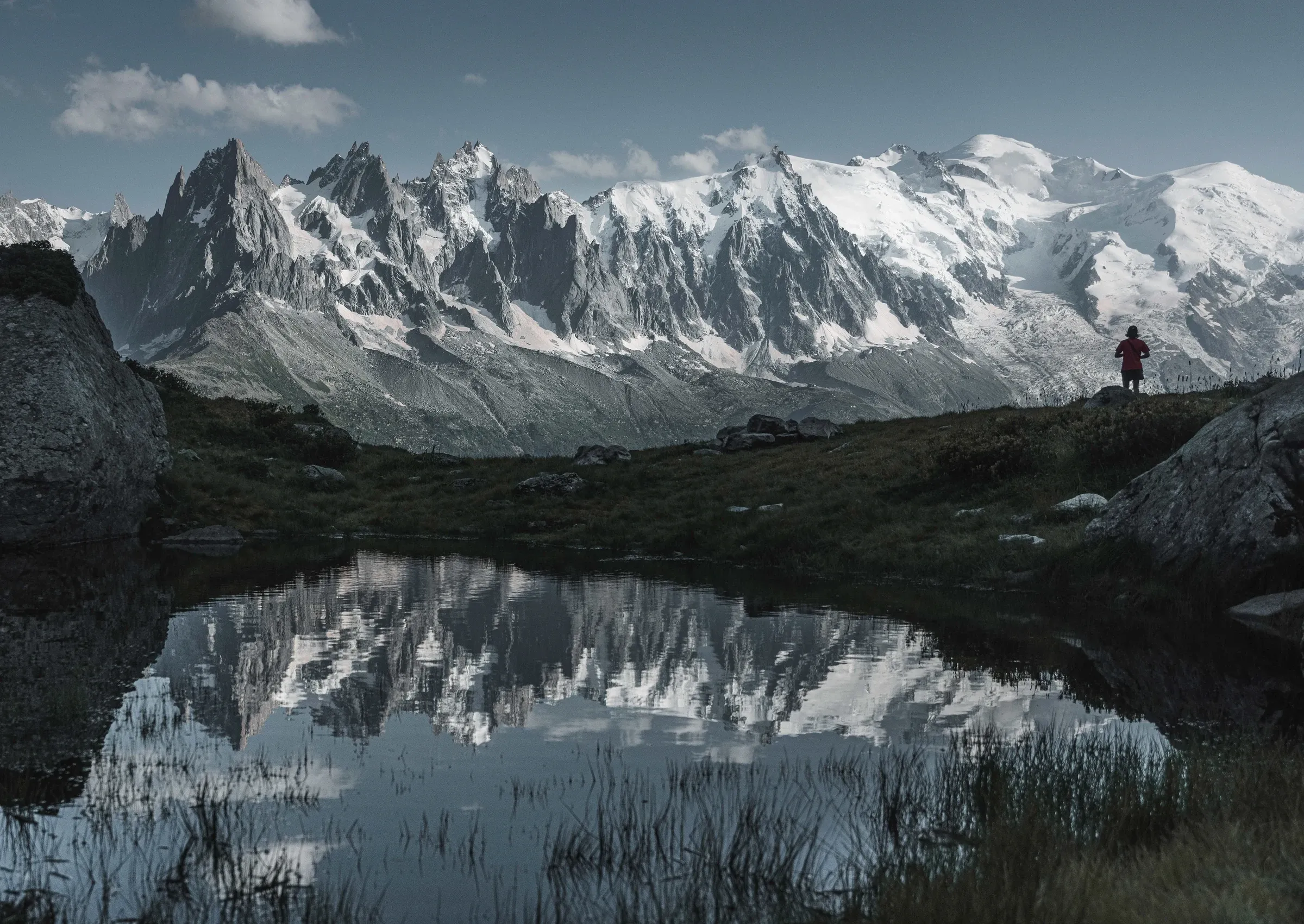 Snow-covered peaks reflected in a mountain lake, with a small figure on the shore