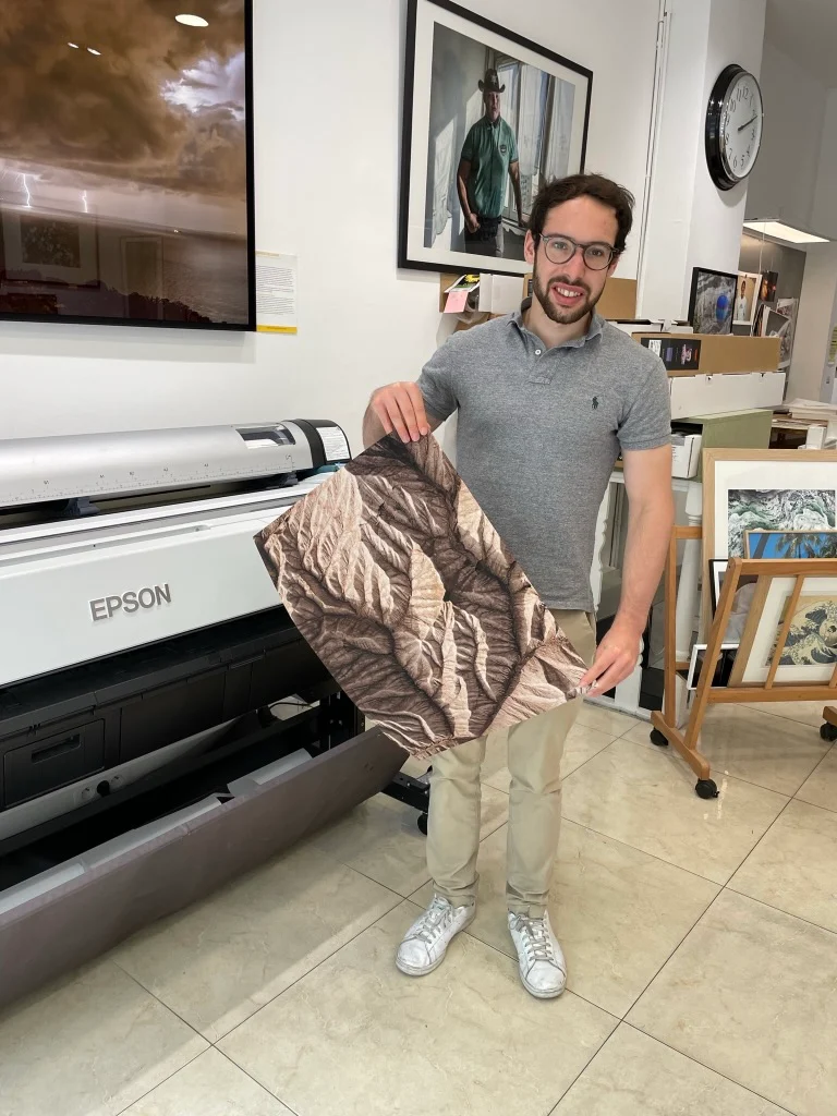 Sam holding a landscape print beside a large-format printer